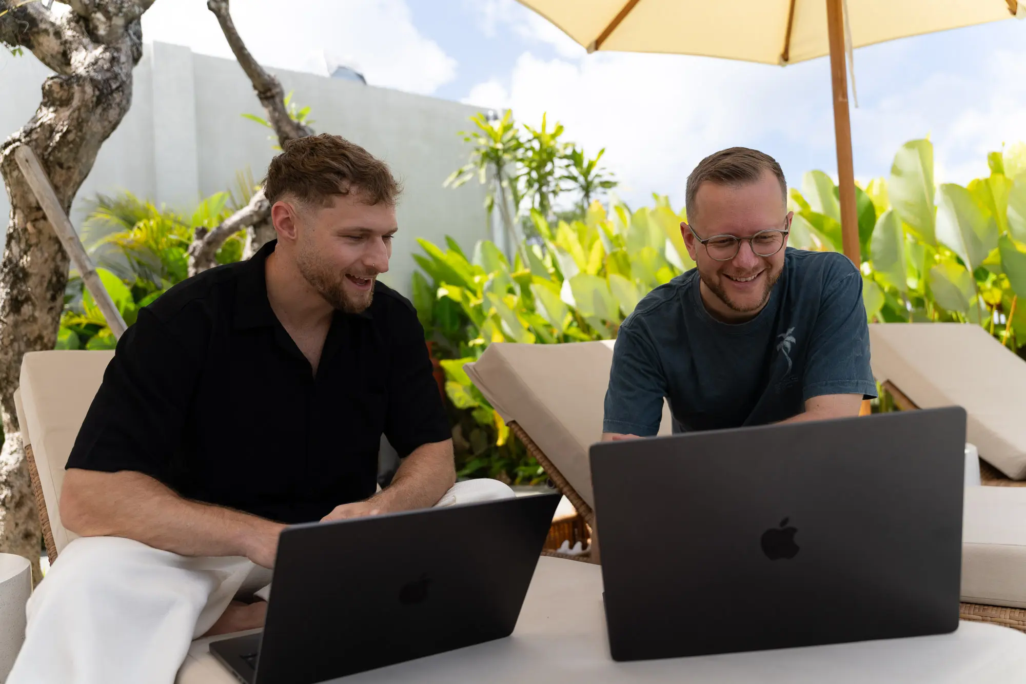 Felix und Tim arbeiten lachend auf Liegen unter Sonnenschirmen