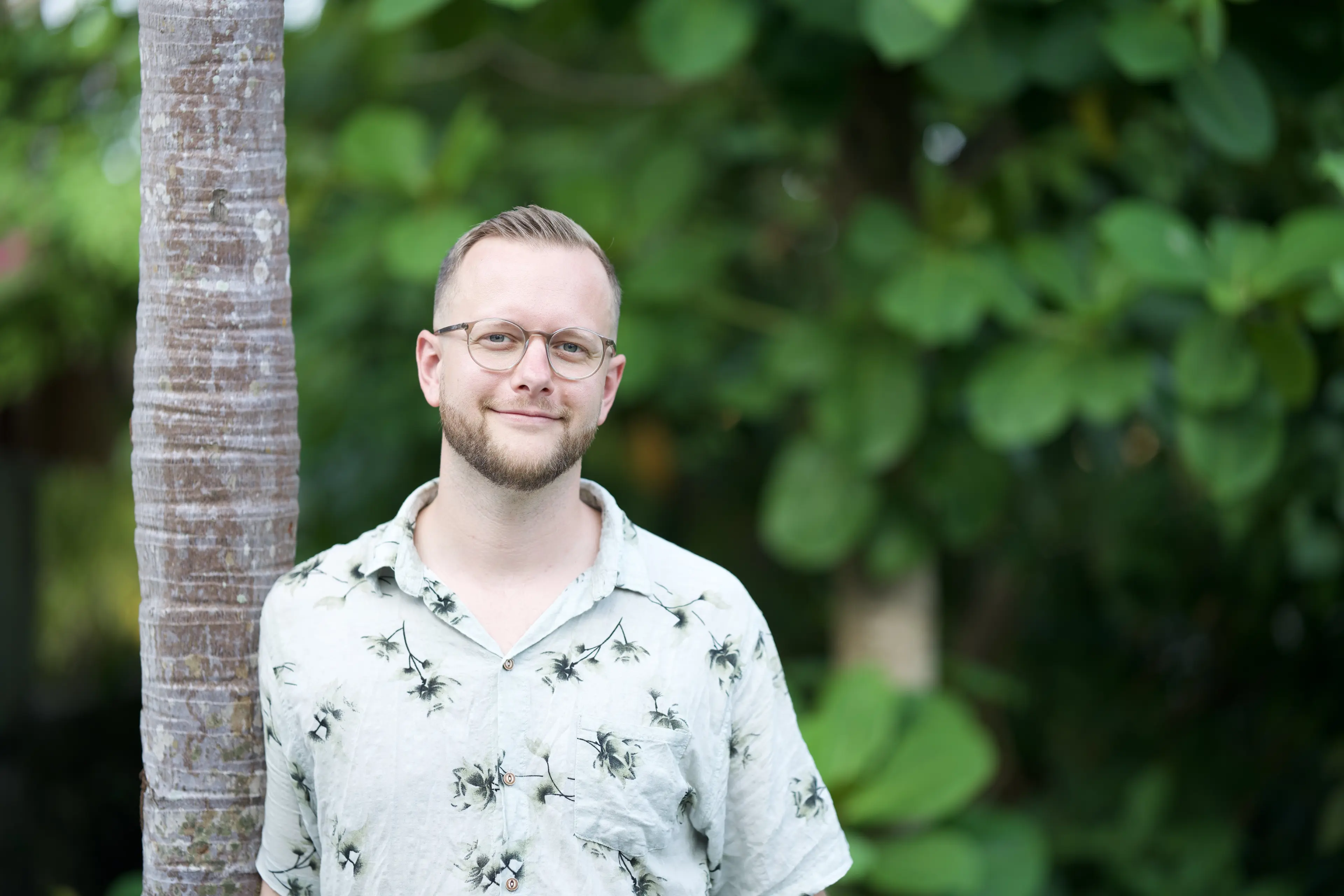 Tim steht lächelnd an einer Palme im Grünen auf Bali