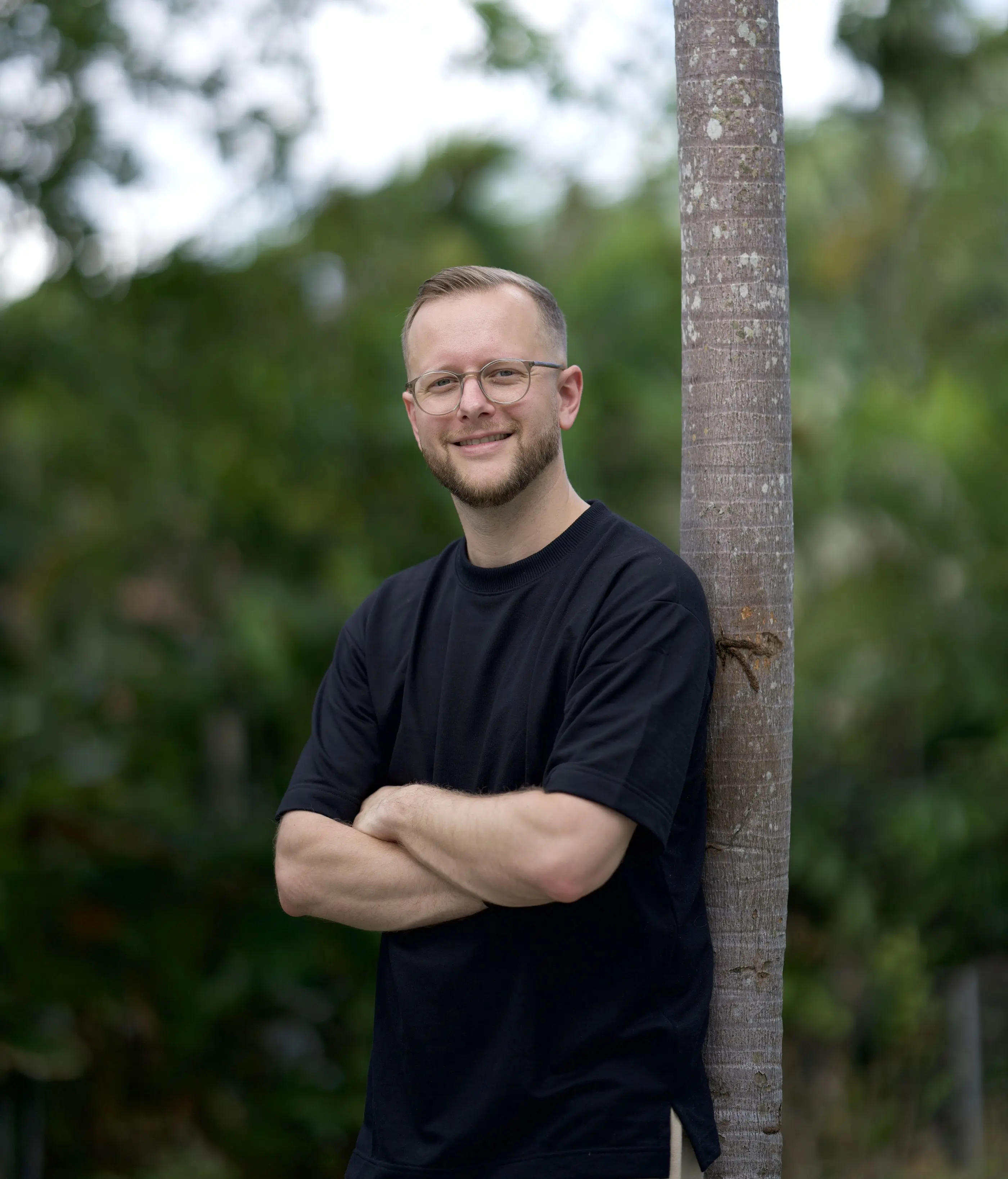 Tim steht mit verschränkten Armen an einer Palme auf Bali