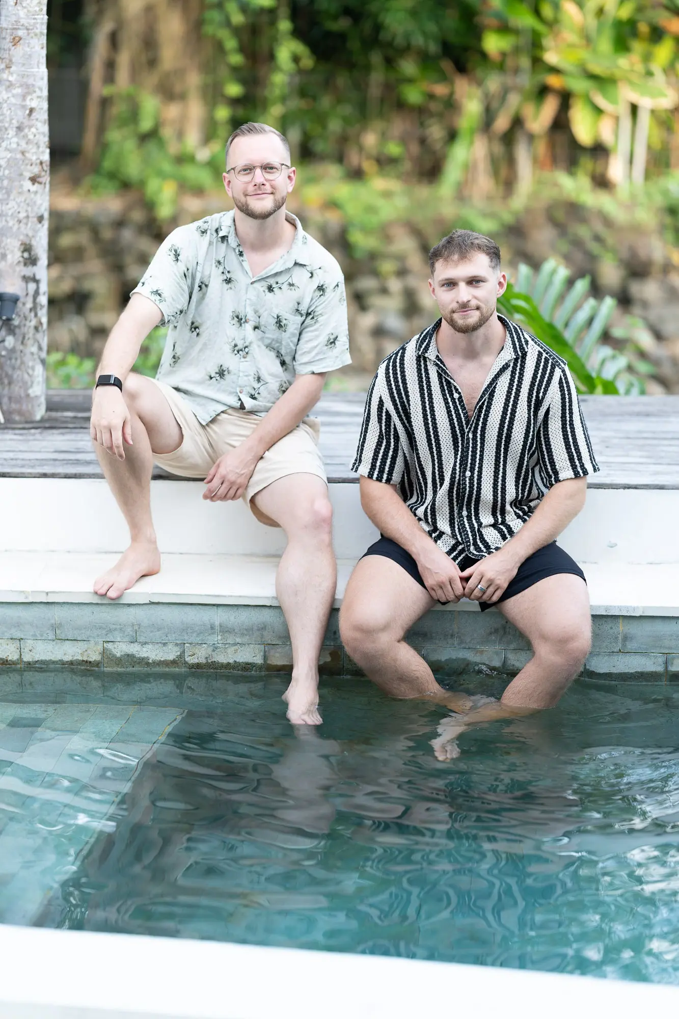 Tim und Felix sitzen am Poolrand und lachen in die Kamera