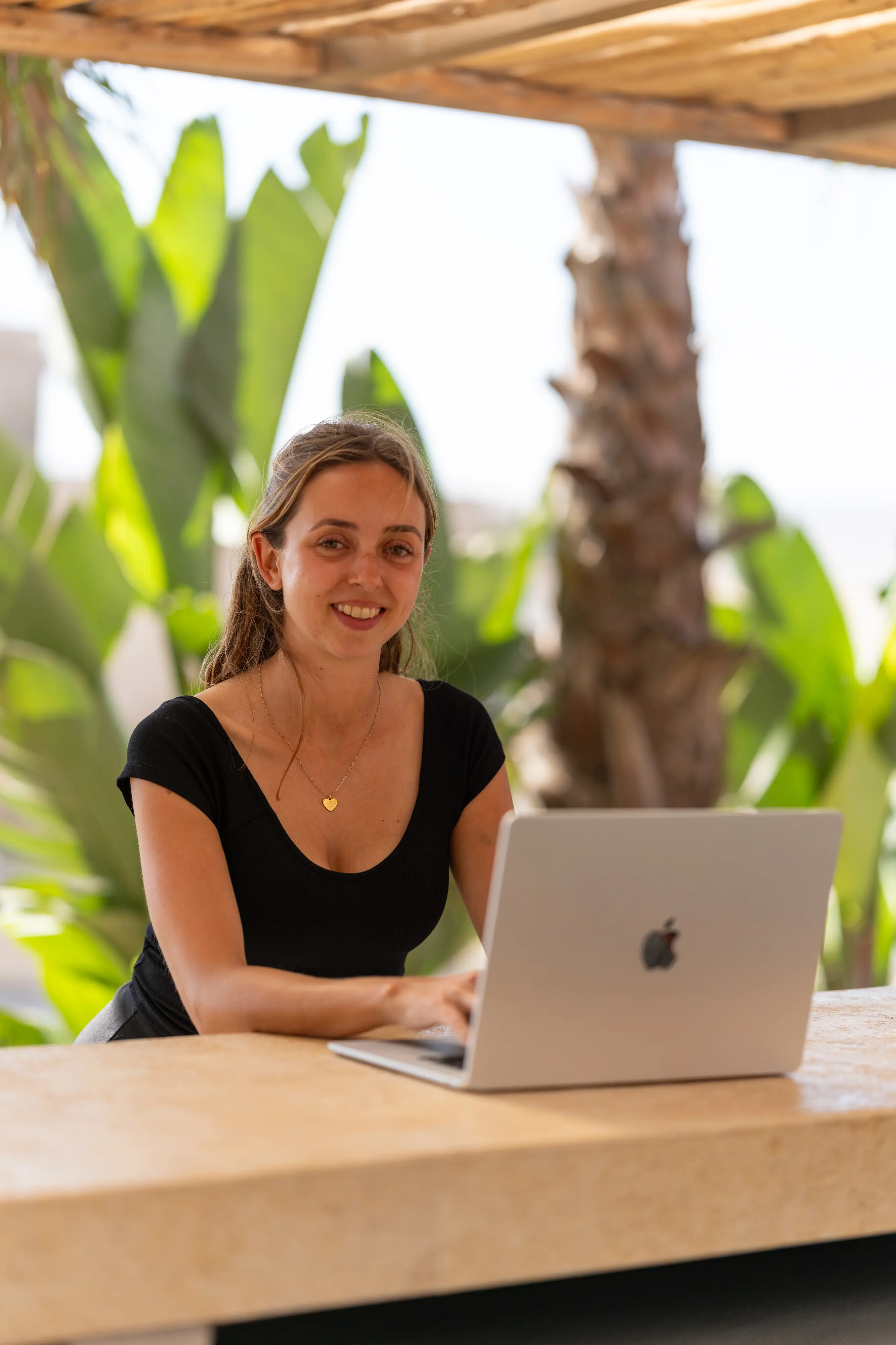 Emma lächelt am Laptop vor Palmen