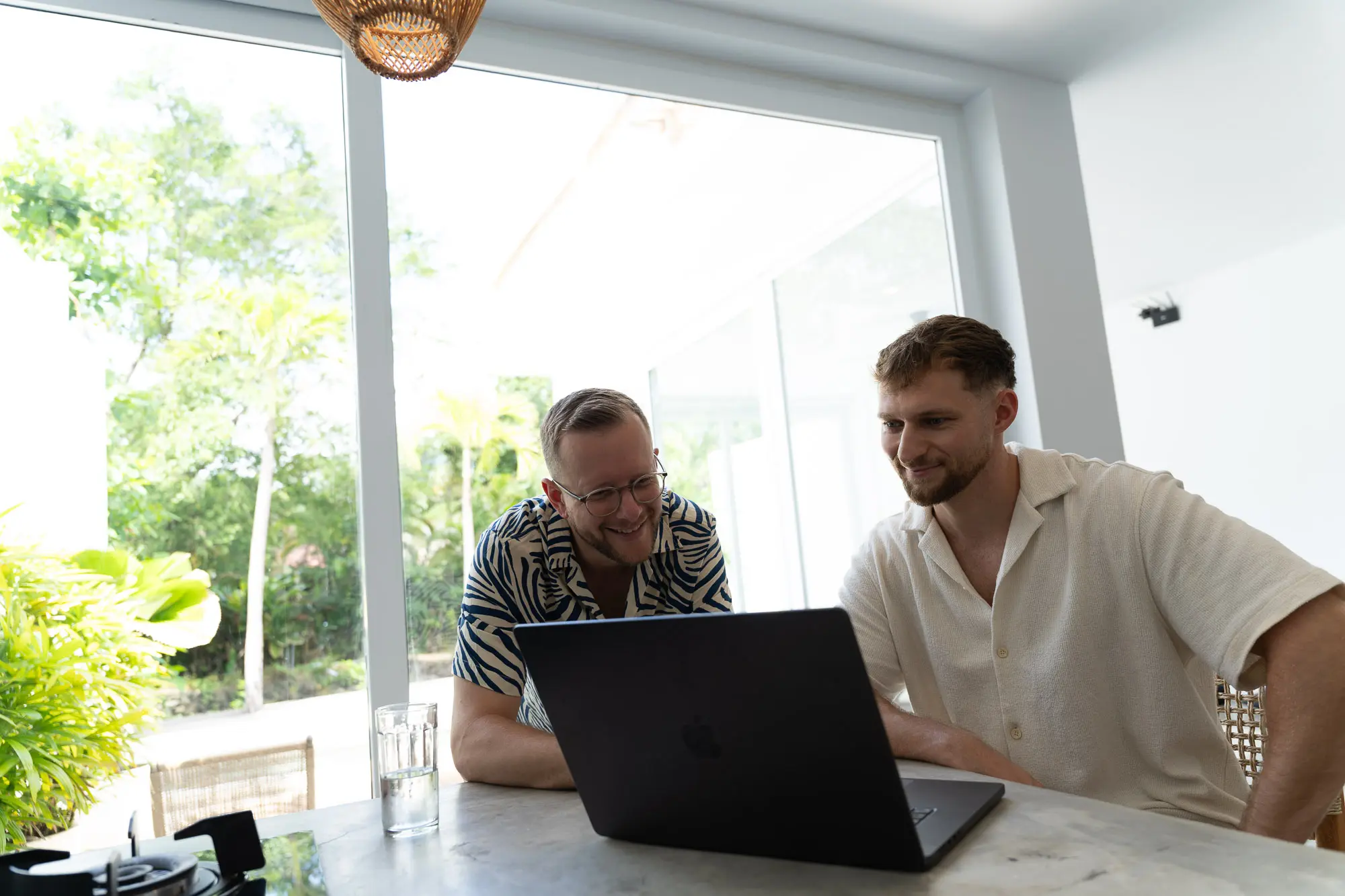 Tim und Felix schauen gemeinsam auf einen Laptop an einem hellen Fenster auf Bali