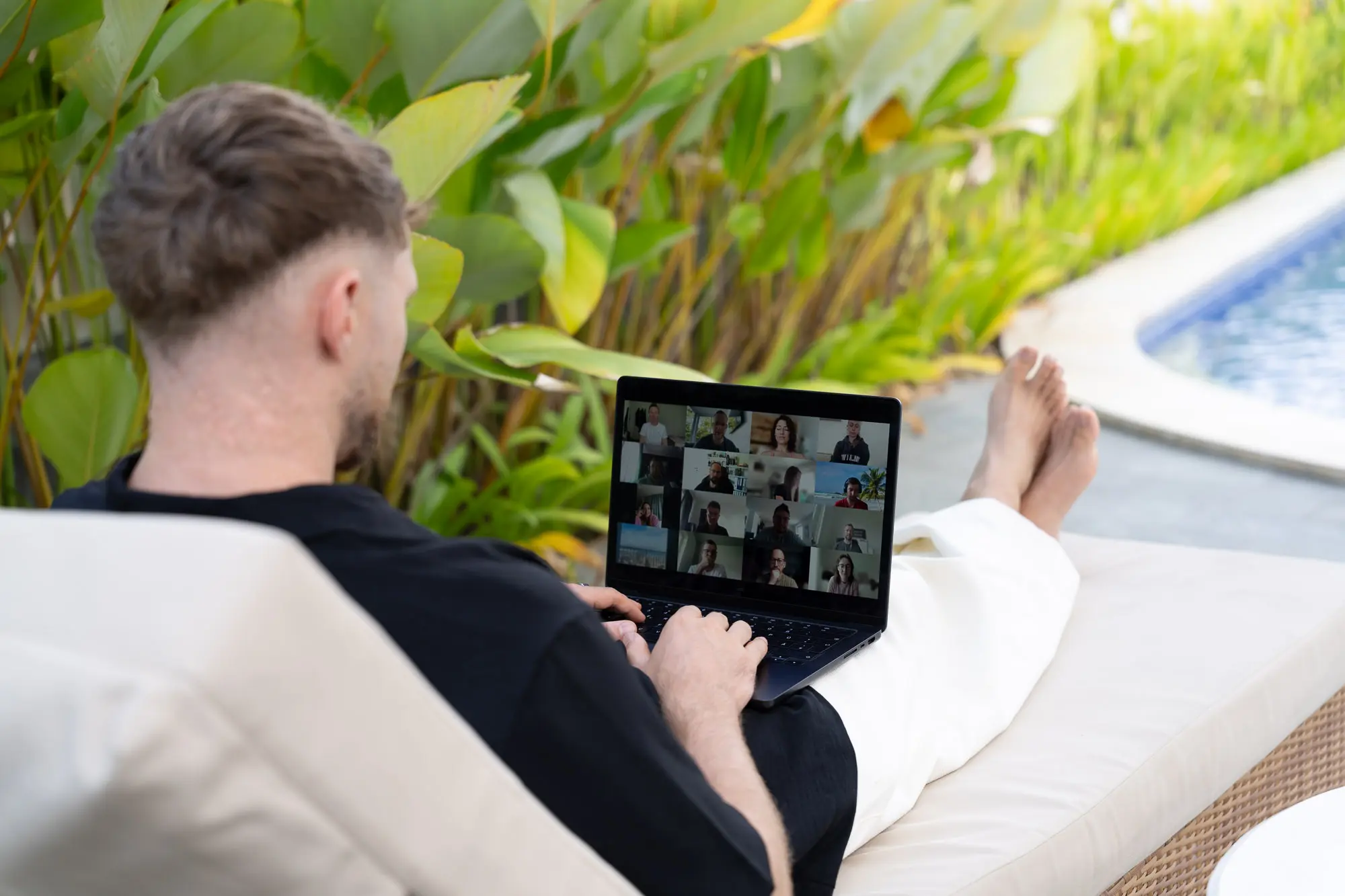 Videocall am Laptop auf einer Poolliege, umgeben von tropischen Pflanzen