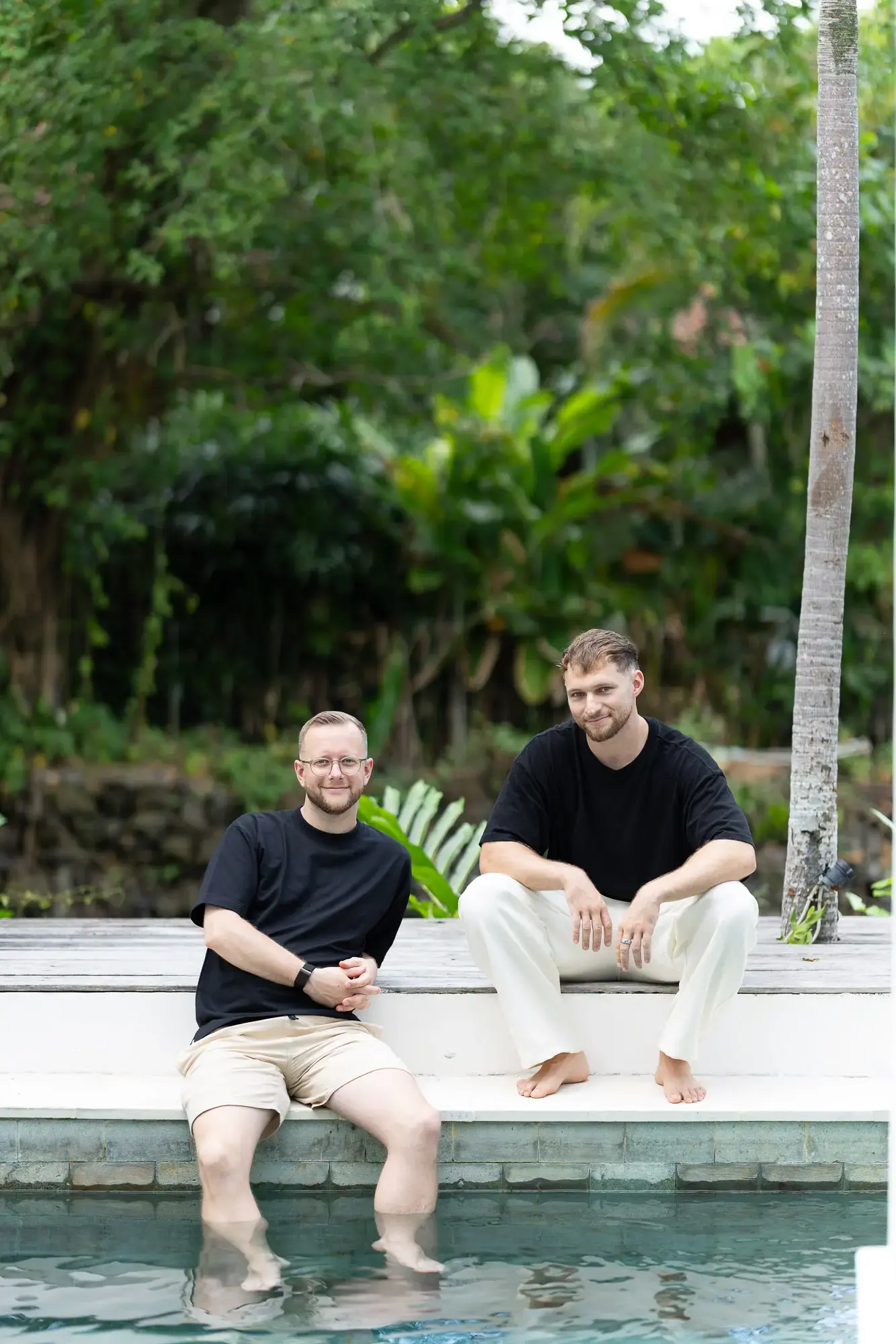 Felix und Tim sitzen mit den Füßen im Pool vor dichtem Grün